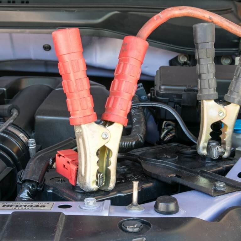 שני מהדקי כבלי הצתה באדום ובשחור מחוברים למסופי מצבר בתוך תא מנוע